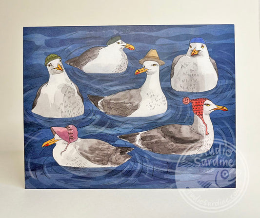 A square art print or card featuring an illustration of six seagulls floating on blue water, each wearing a different colored knit hat. The print is photographed against a plain off-white background.