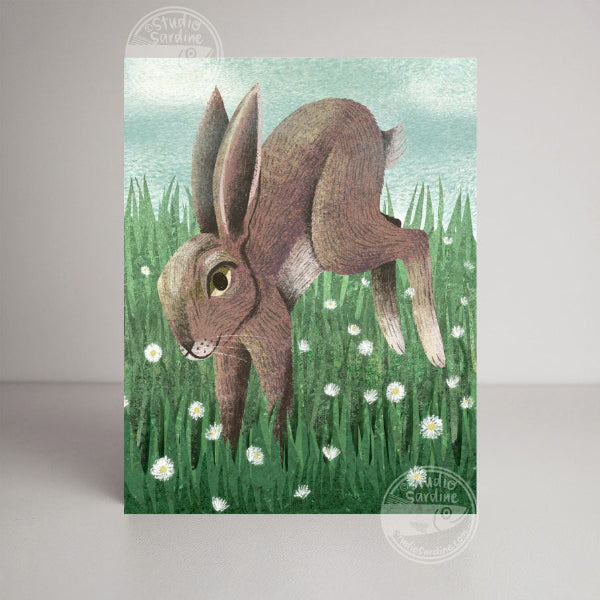 Illustration of a rabbit in a grassy field with flowers on a greeting card.